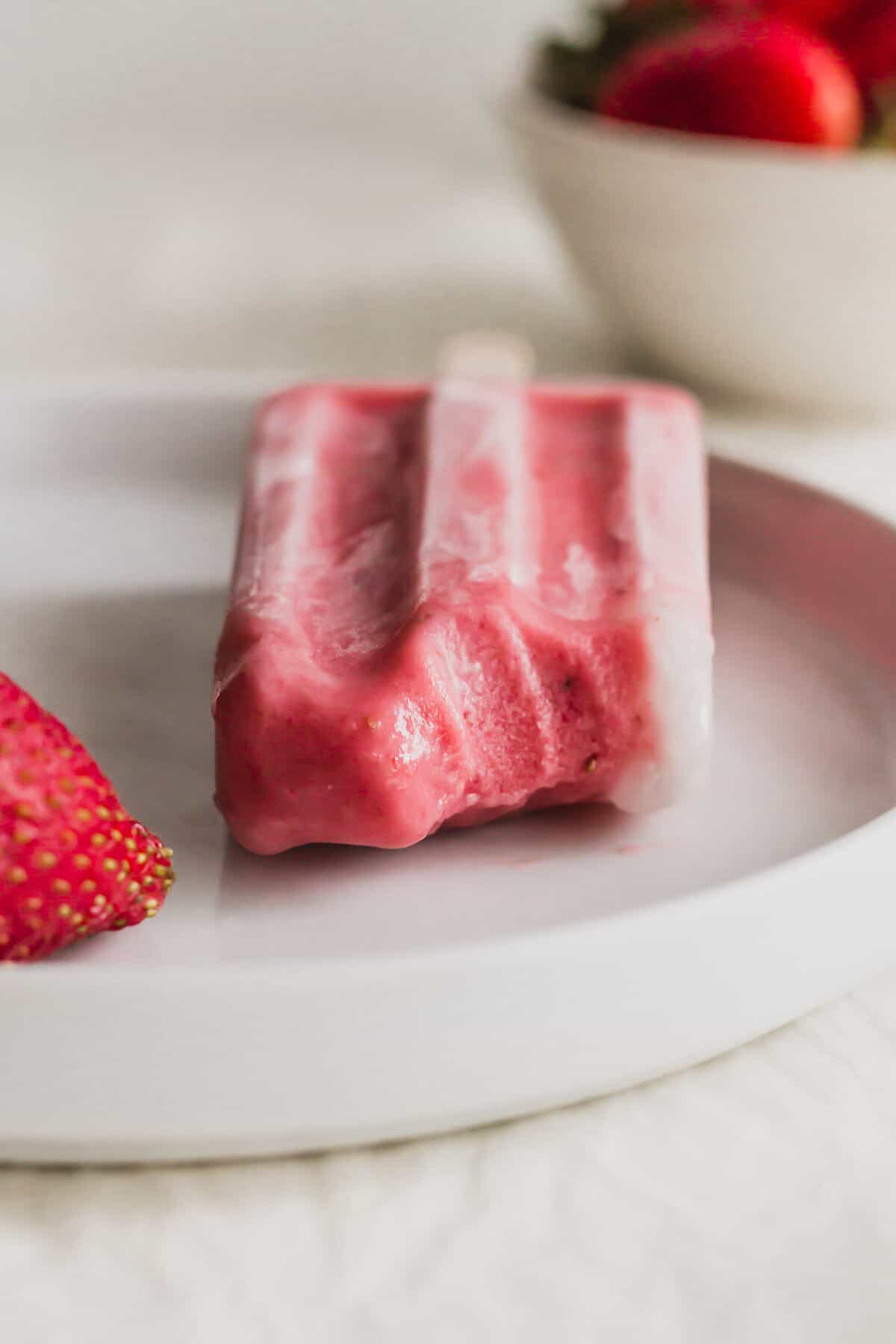Half bitten strawberry sago popsicle, revealing interior on a white plate.